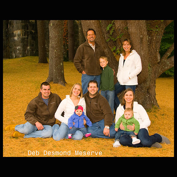 large family sitting on the grass and pine needles in a wooded area